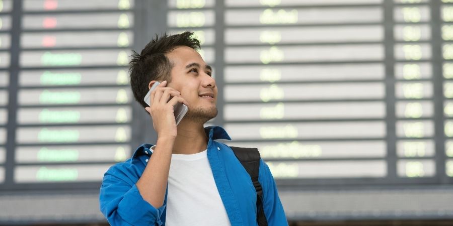 Joven en aeropuerto de NZ hablando por teléfono mientras espera su vuelo
