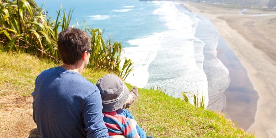 Padre e hijo viviendo en Nueva Zelanda sentados viendo la playa 
